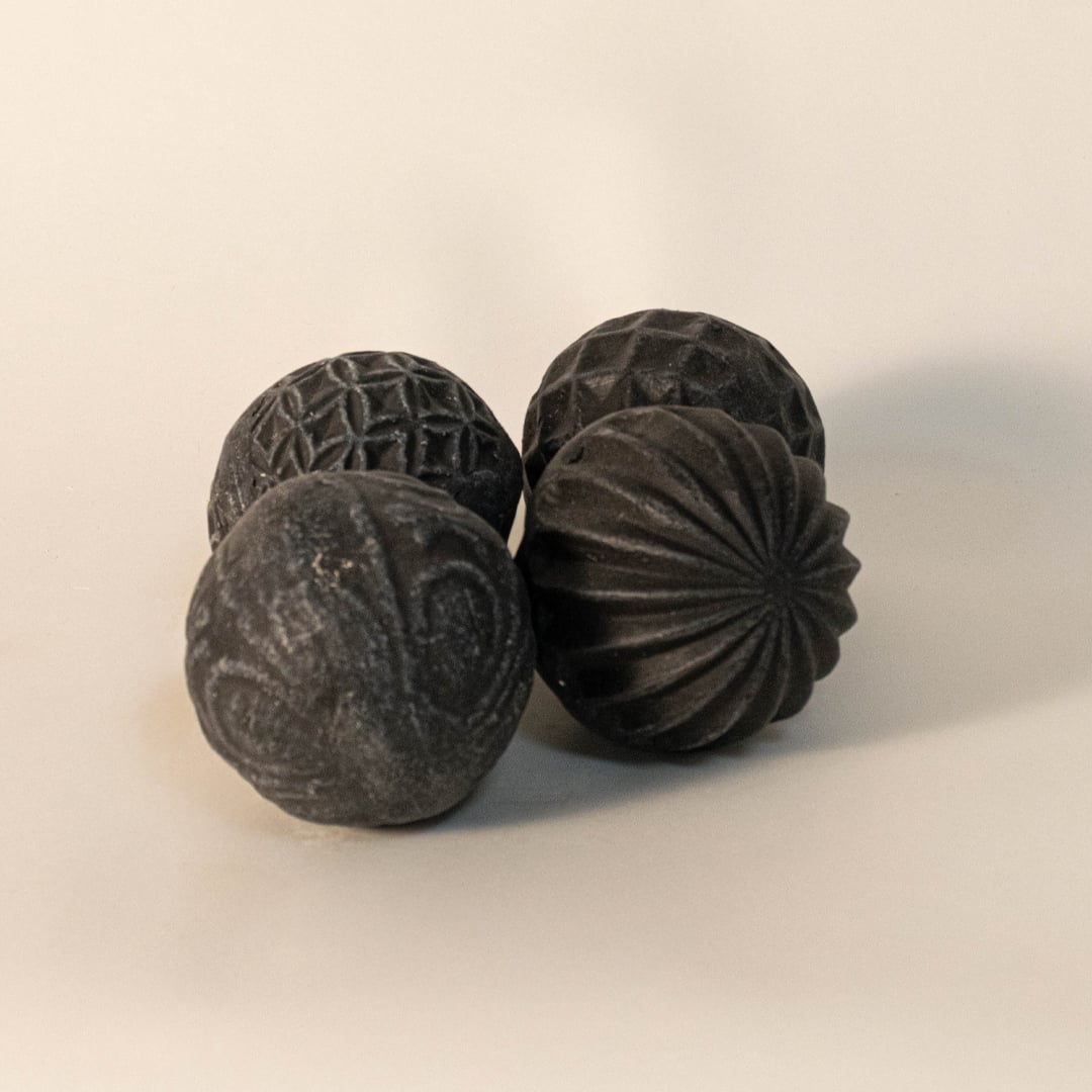 Black carved ball on plain white background showcasing organic spherical form and matte handcrafted finish.