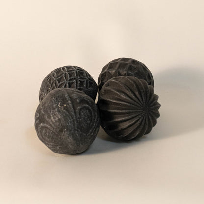 Black carved ball on plain white background showcasing organic spherical form and matte handcrafted finish.
