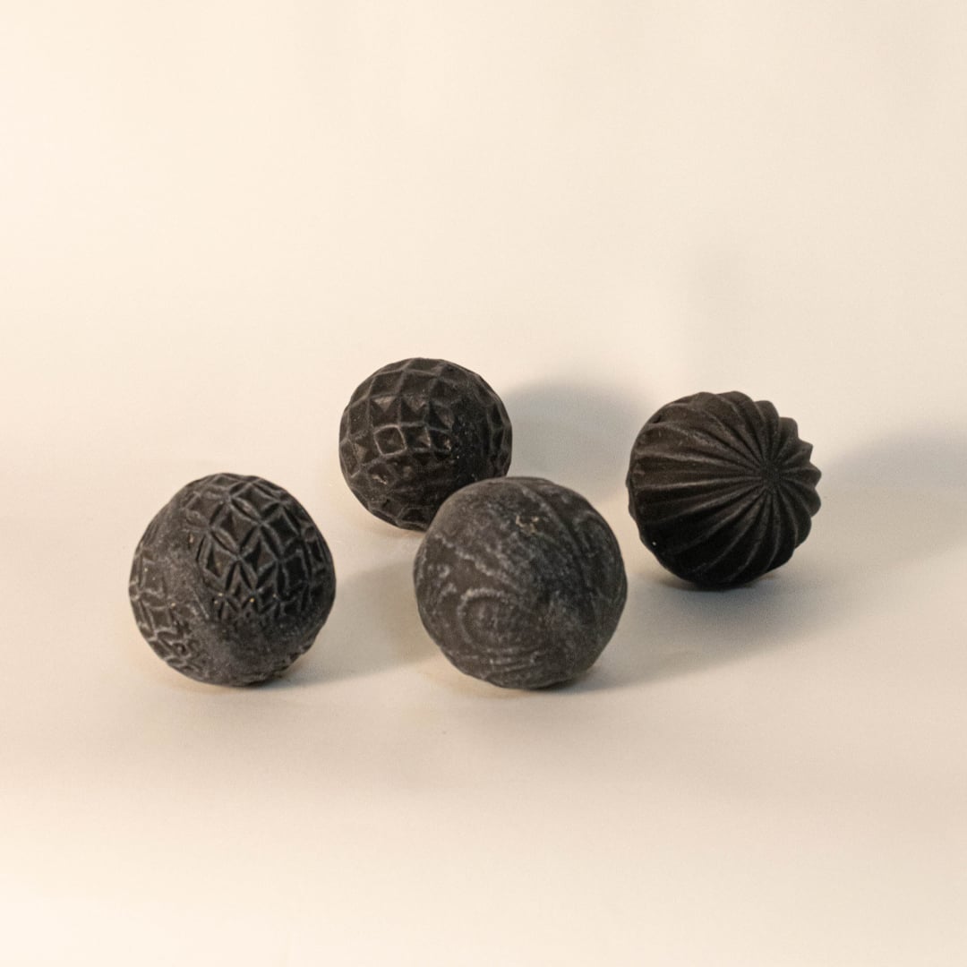 Four black carved ceramic balls with unique handmade designs displayed on white background for modern interior accents.