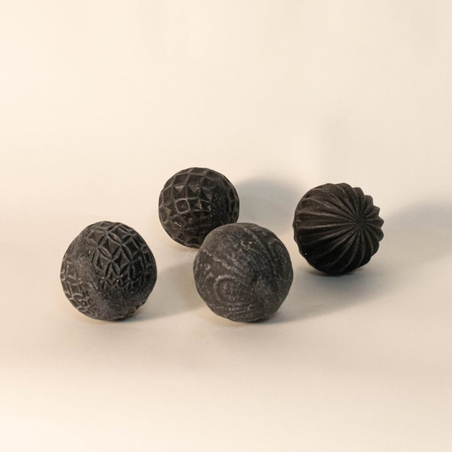 Four black carved ceramic balls with unique handmade designs displayed on white background for modern interior accents.