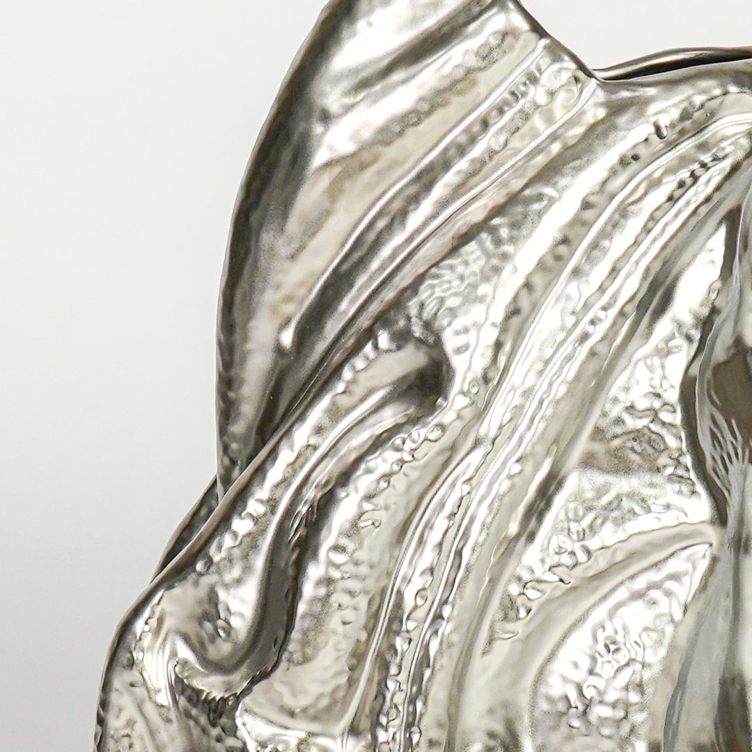 Close up of silver sculptural decor showing fluid wave like texture reflective metallic finish and artistic modern form.