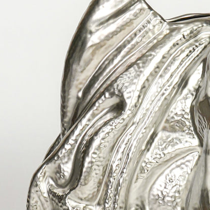Close up of silver sculptural decor showing fluid wave like texture reflective metallic finish and artistic modern form.
