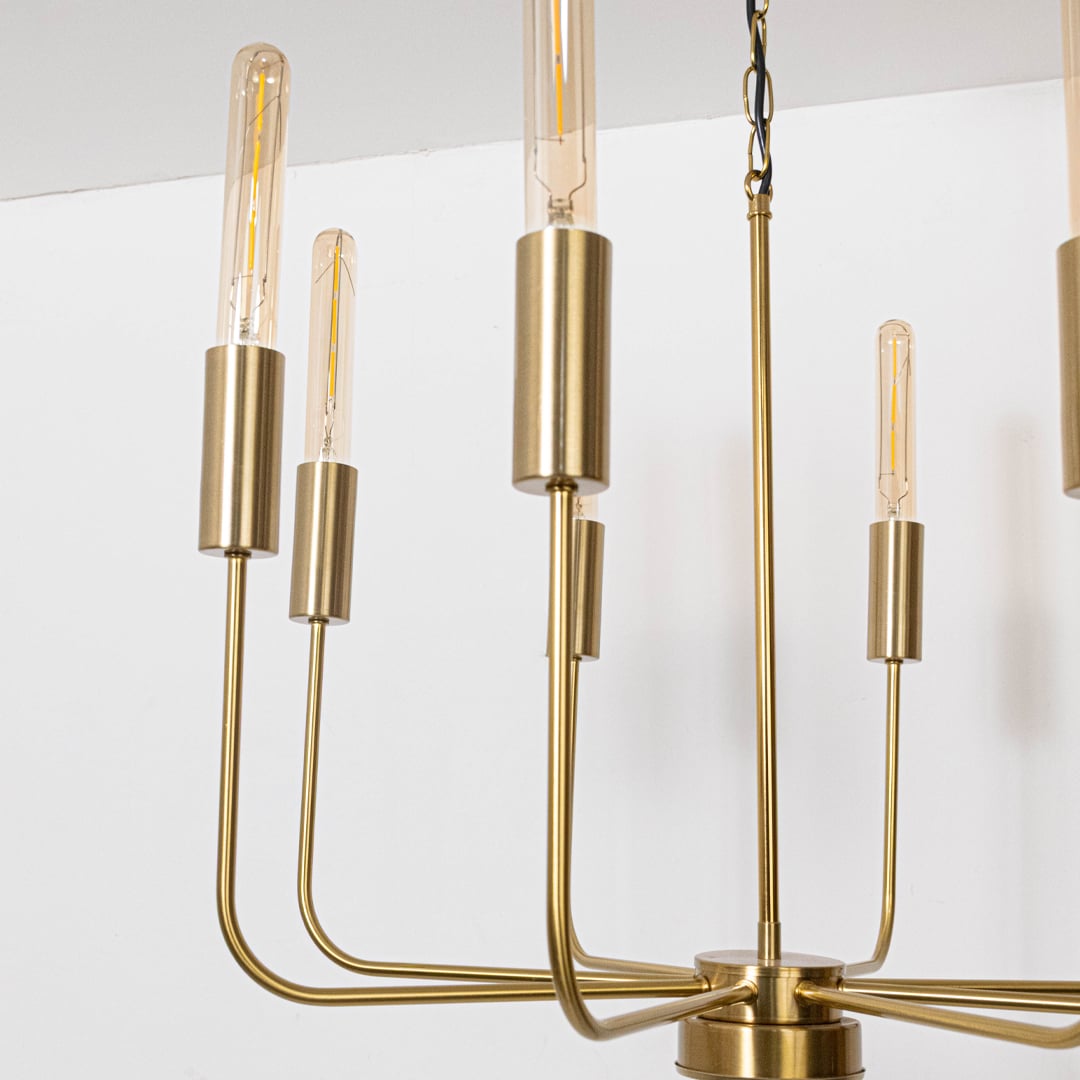 Detailed closeup of exposed vintage Edison tube bulb with brass gold cylindrical socket on contemporary chandelier curved arm.