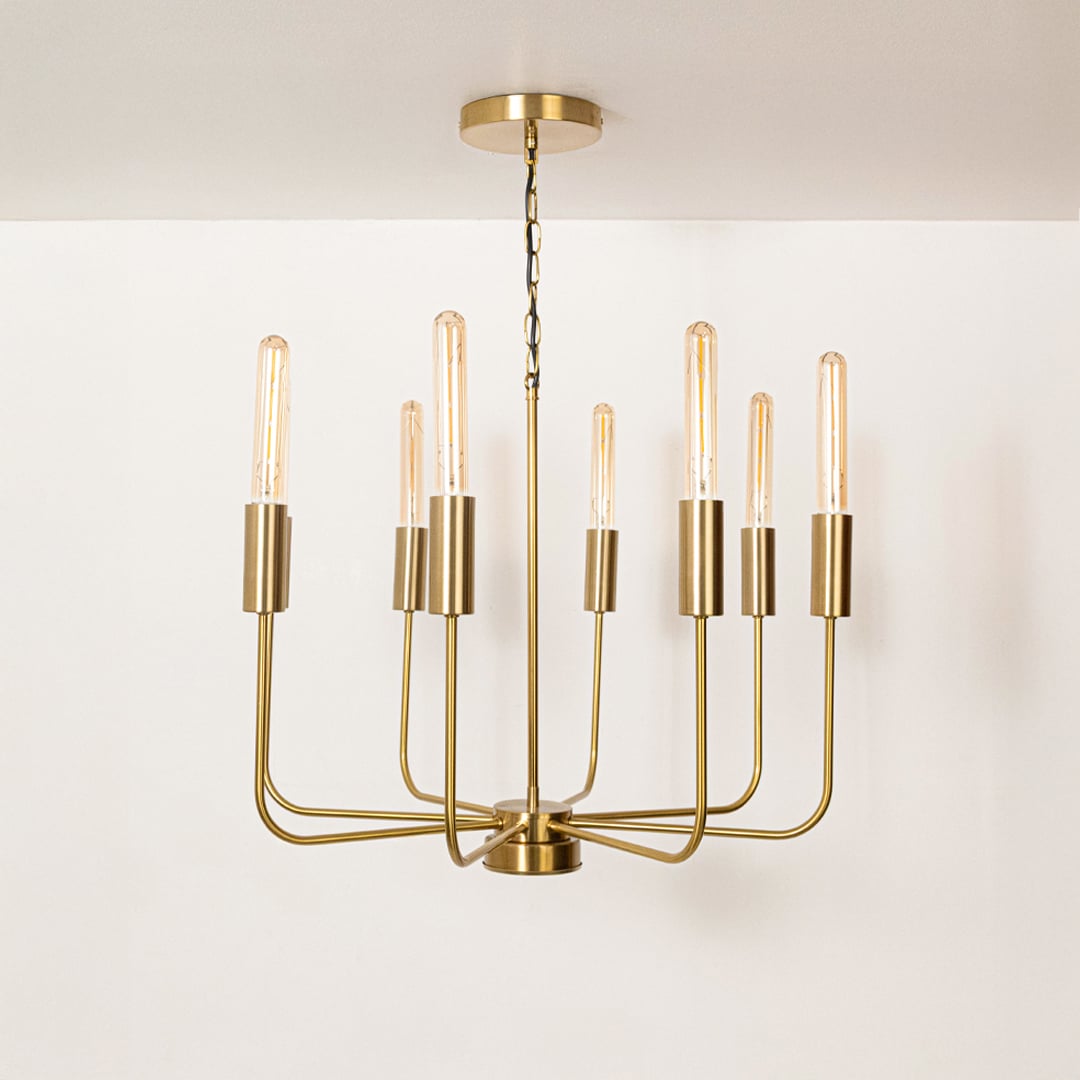 Contemporary brass gold metal eight arm chandelier with chain and Edison tube bulb sockets turned off on white background.