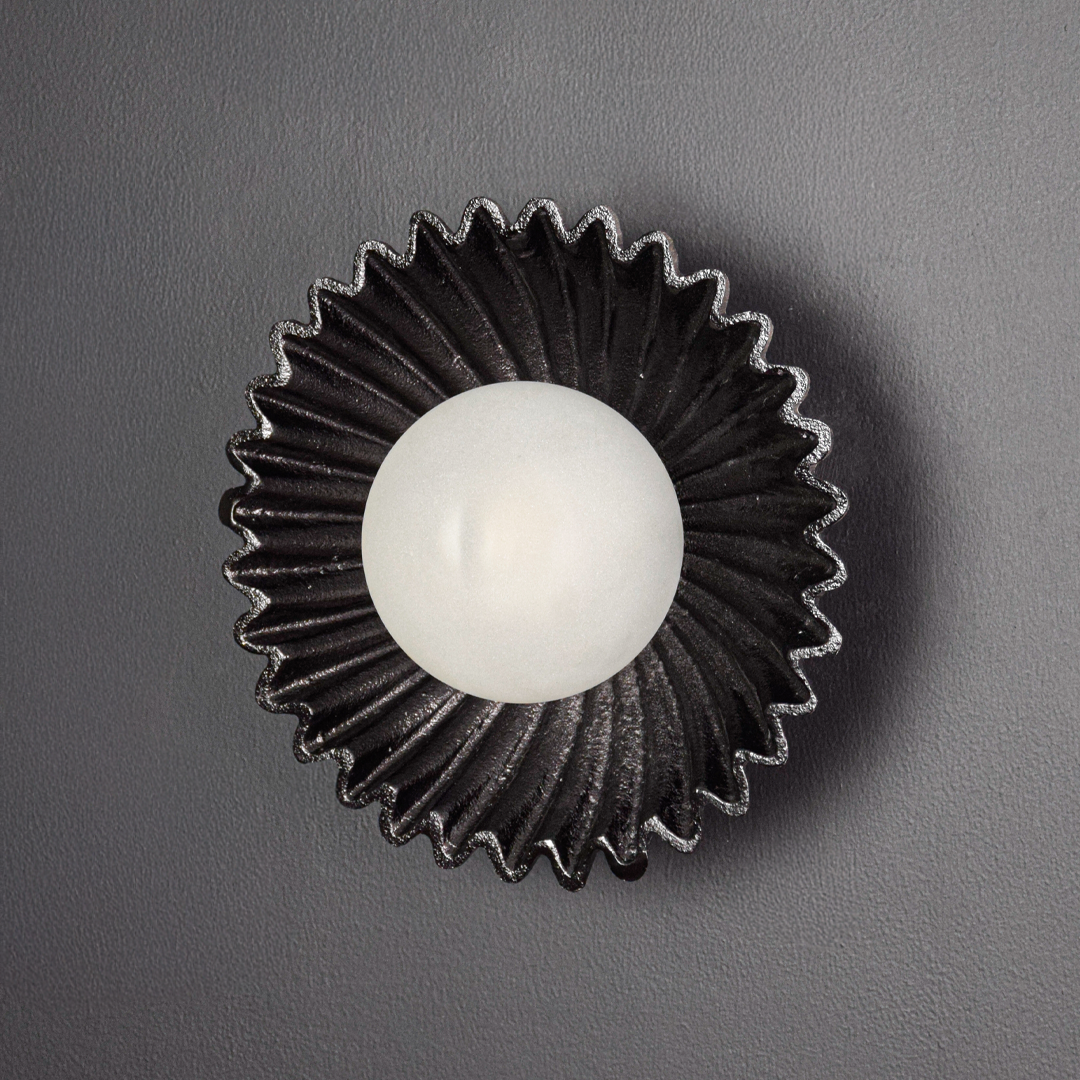 Wall light displayed switched off on a deep black background emphasizing the sculptural silhouette textured metal surface and bold contrast.