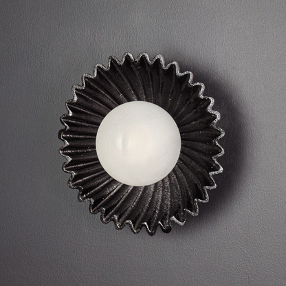 Wall light displayed switched off on a deep black background emphasizing the sculptural silhouette textured metal surface and bold contrast.