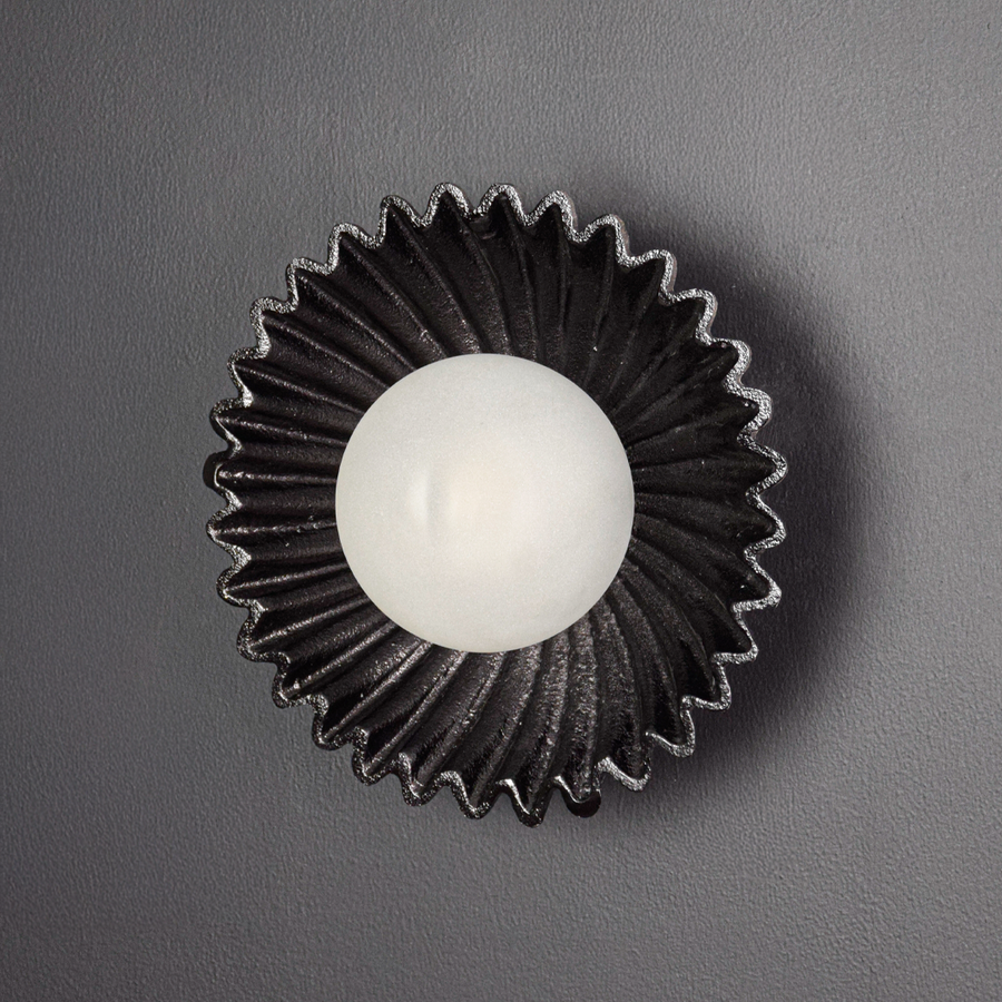 Wall light displayed switched off on a deep black background emphasizing the sculptural silhouette textured metal surface and bold contrast.