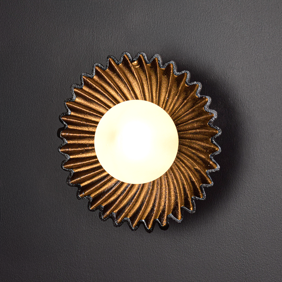 Wall light illuminated on a black background creating a dramatic warm halo that highlights the sculpted metal form and elegant modern appeal.
