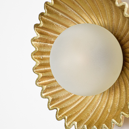 Wall light closeup highlighting rippled gold metal texture with smooth frosted glass globe showcasing premium craftsmanship and elegant finish.