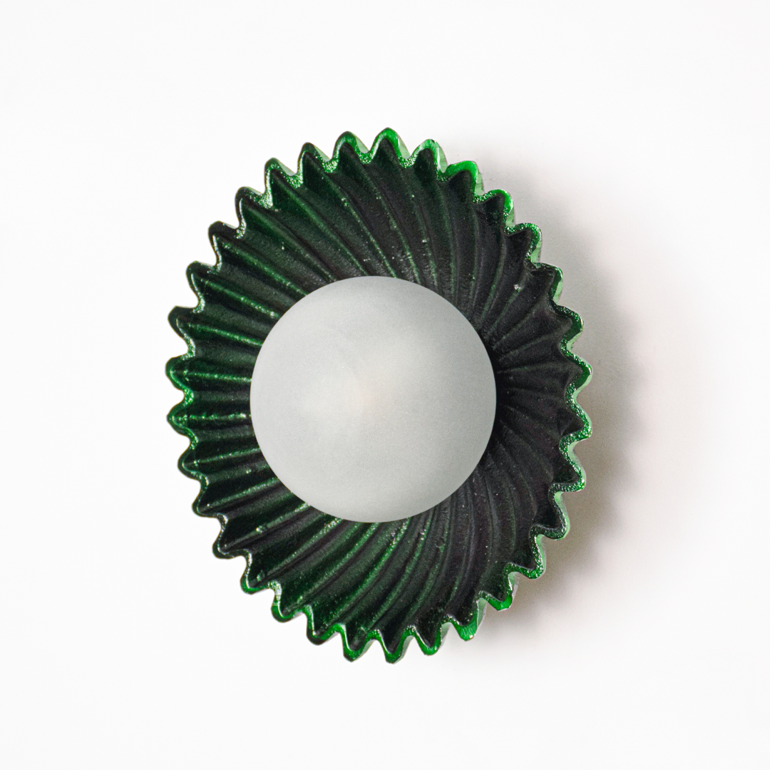 Wall light off on white background featuring deep green fluted metal plate with centered glass globe for minimalist product presentation.