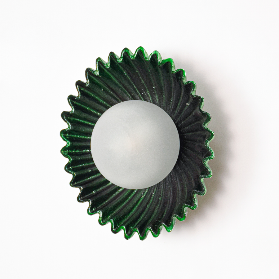 Wall light off on white background featuring deep green fluted metal plate with centered glass globe for minimalist product presentation.
