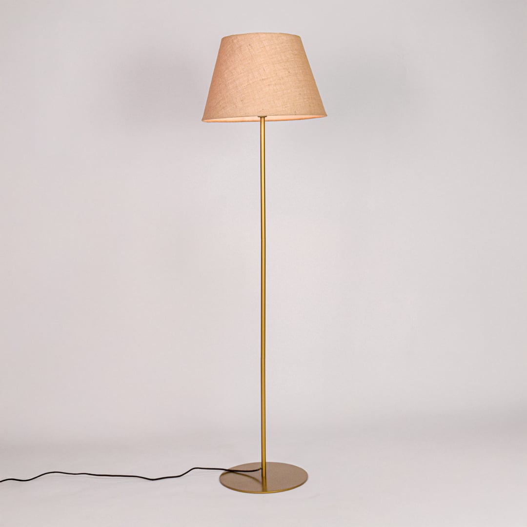 Gold metal floor lamp glowing warmly through beige fabric shade on white background for cozy home Decor.