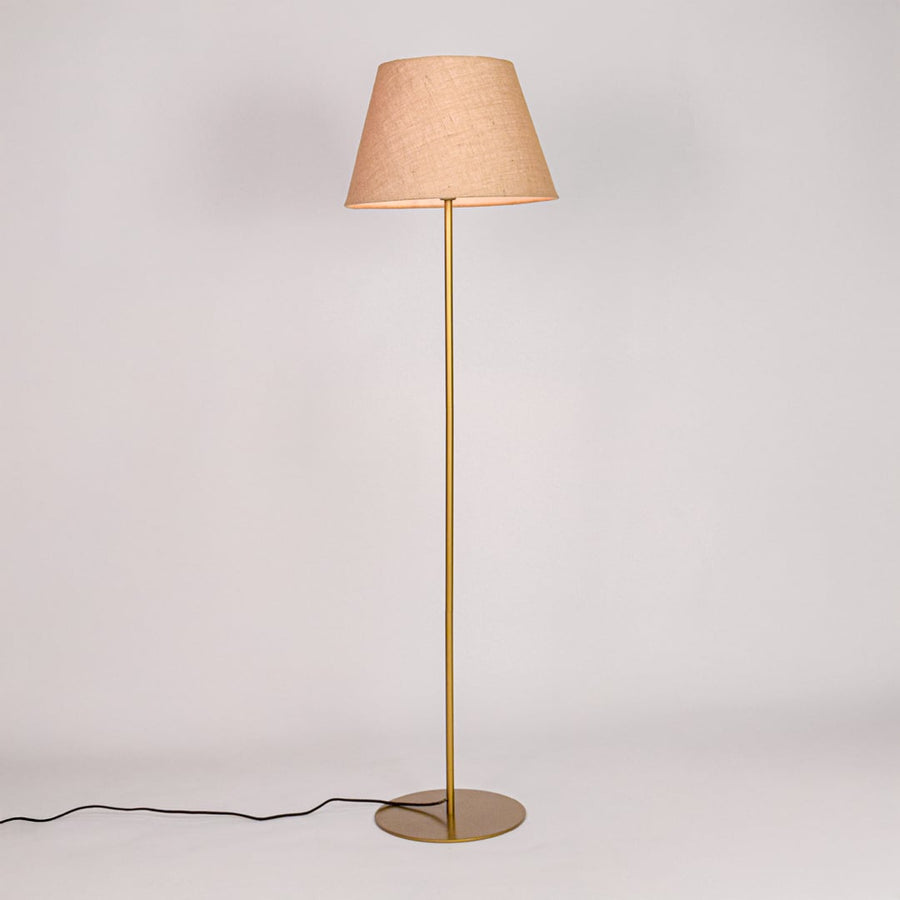 Gold metal floor lamp glowing warmly through beige fabric shade on white background for cozy home Decor.