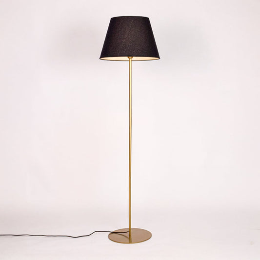 Gold metal floor lamp glowing warmly through black fabric shade on white background for cozy home Decor.