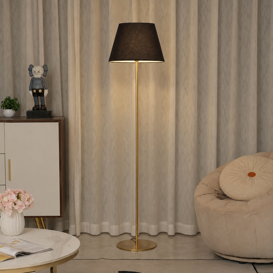 Black fabric shade floor lamp with brass stem creating warm ambient lighting beside lounge chair in modern interiors.