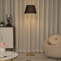 Black fabric shade floor lamp with brass stem creating warm ambient lighting beside lounge chair in modern interiors.
