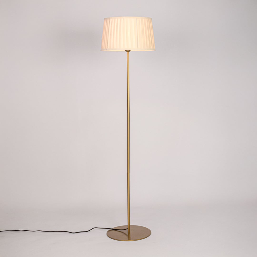 Gold floor lamp illuminated with warm glow through pleated white shade against plain white background.