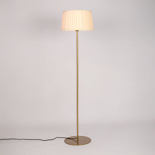 Gold floor lamp illuminated with warm glow through pleated white shade against plain white background.