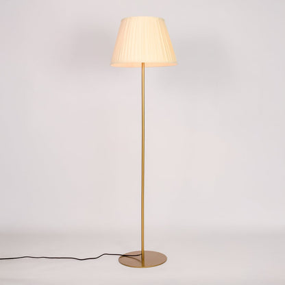 Gold metal floor lamp glowing warmly through pleated cream fabric shade on white background for cozy home Decor.