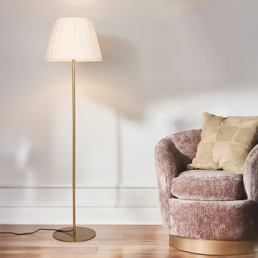 Modern gold metal floor lamp with pleated white fabric shade placed in living room corner for warm ambient lighting Decor.