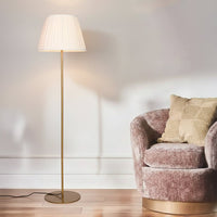 Modern gold metal floor lamp with pleated white fabric shade placed in living room corner for warm ambient lighting Decor.