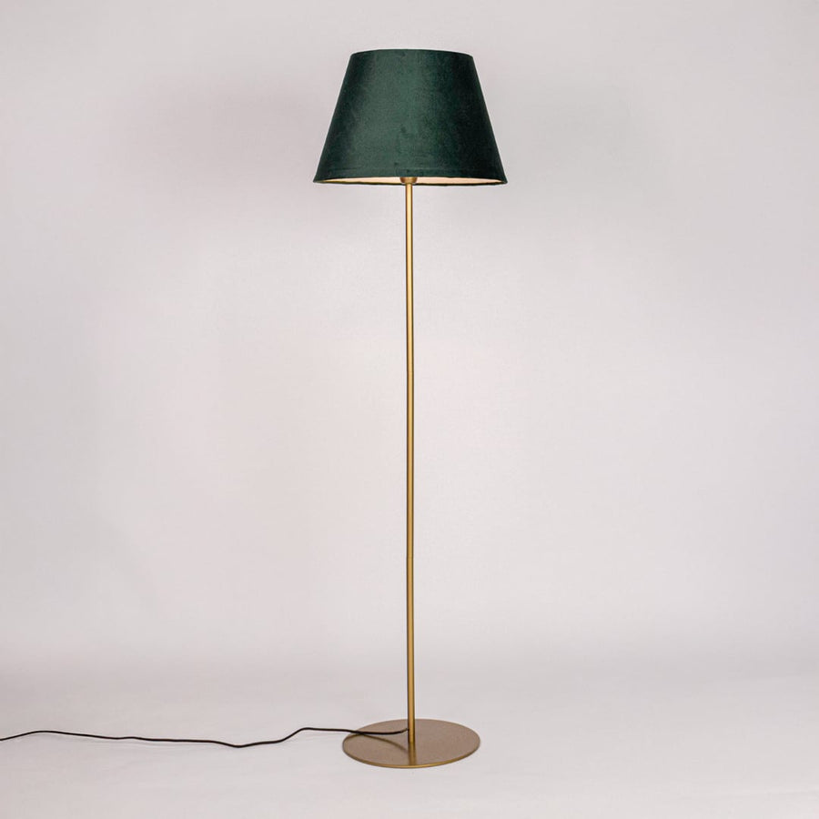 Gold metal floor lamp with green fabric shade illuminated on white background for warm ambient home lighting Decor.