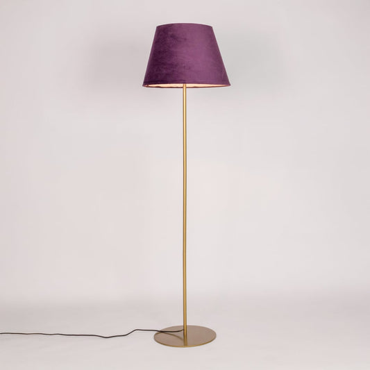 Gold metal floor lamp glowing warmly through purple fabric shade on white background for cozy home Decor.