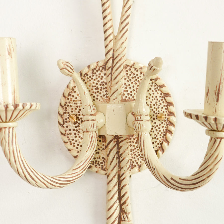 A close-up of a distressed cream and brown wall sconce with twisted rope-style arms and a circular patterned backplate.