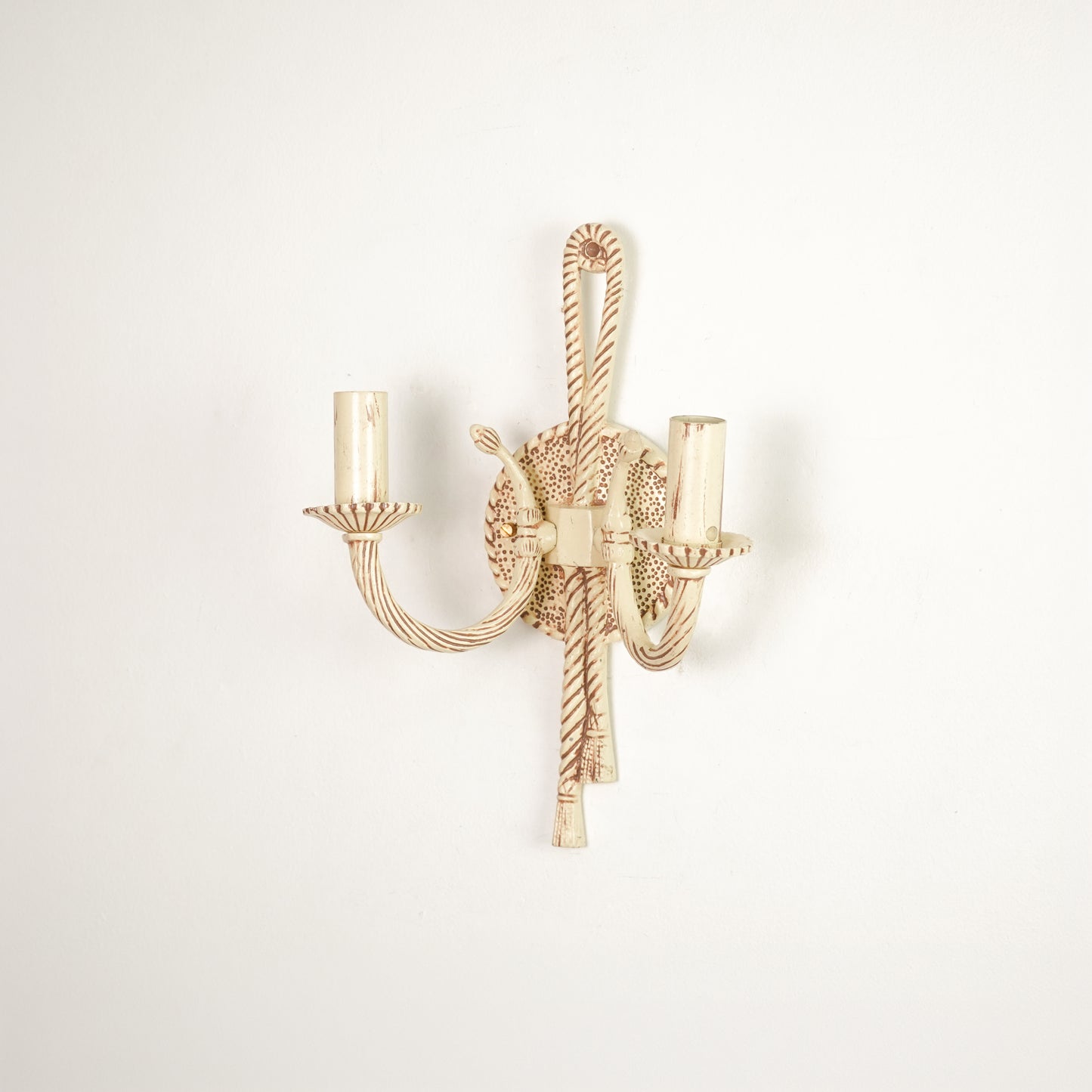 A single wall-mounted candelabra-style light fixture with twisted rope details and two candle-shaped bulb sockets, shown against a plain off-white wall.