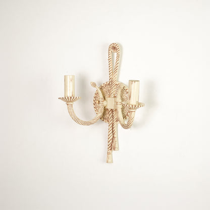 A single wall-mounted candelabra-style light fixture with twisted rope details and two candle-shaped bulb sockets, shown against a plain off-white wall.