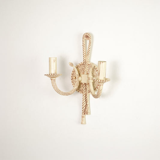 A single wall-mounted candelabra-style light fixture with twisted rope details and two candle-shaped bulb sockets, shown against a plain off-white wall.