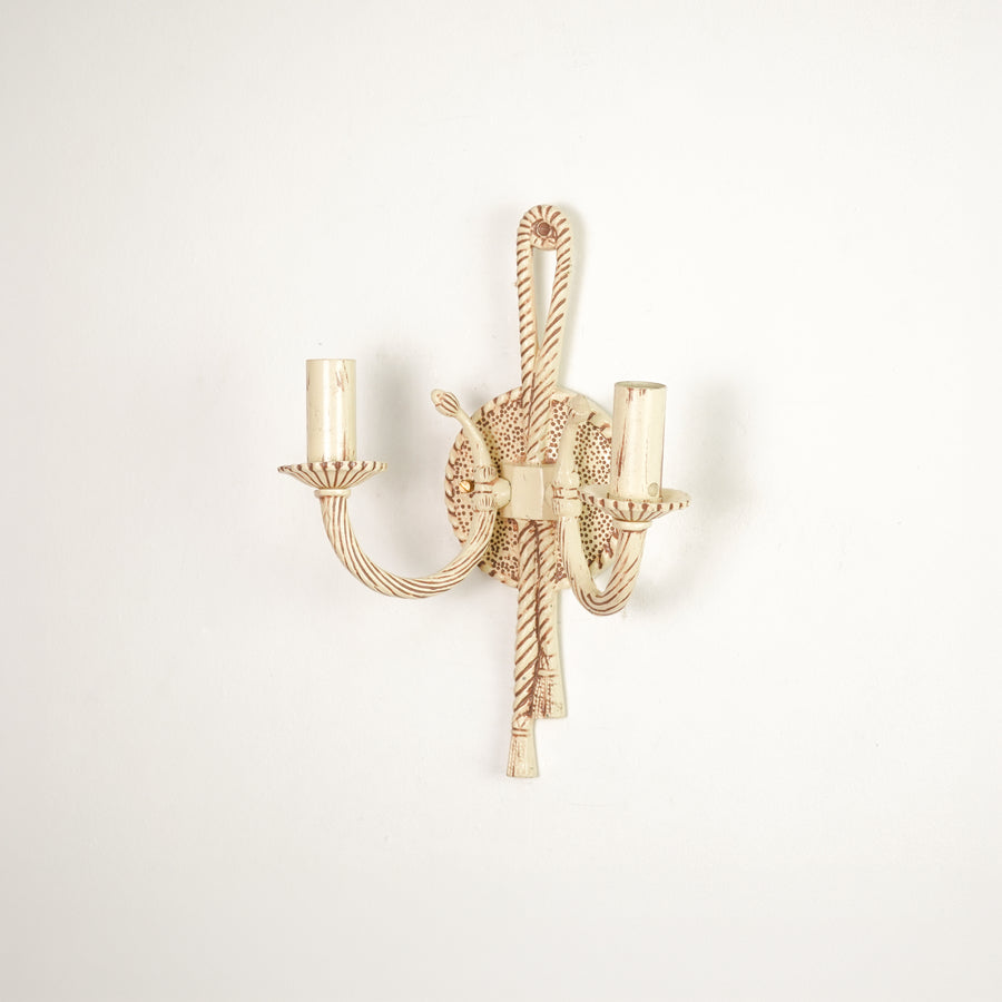 A single wall-mounted candelabra-style light fixture with twisted rope details and two candle-shaped bulb sockets, shown against a plain off-white wall.