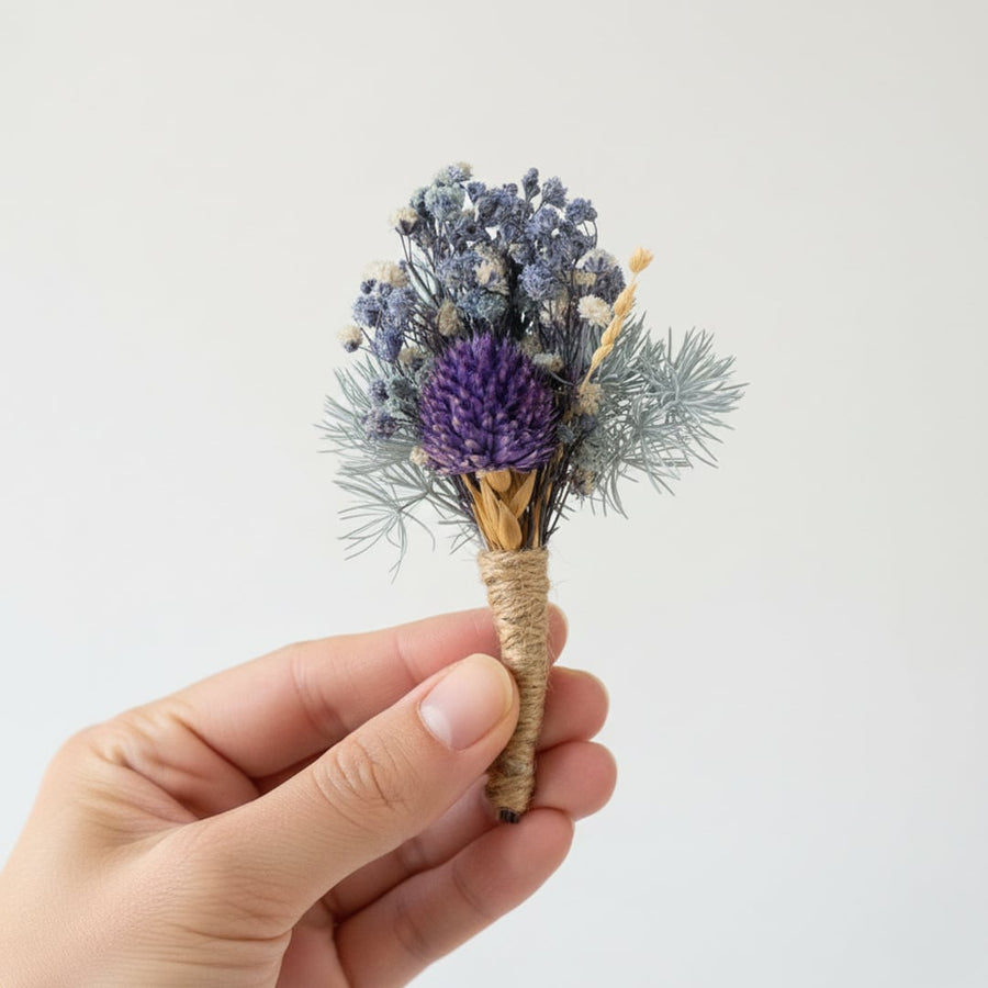 Dried mini floral bouquet with purple blue and neutral tones held by hand on white background highlighting layered texture natural beauty and decor styling charm.