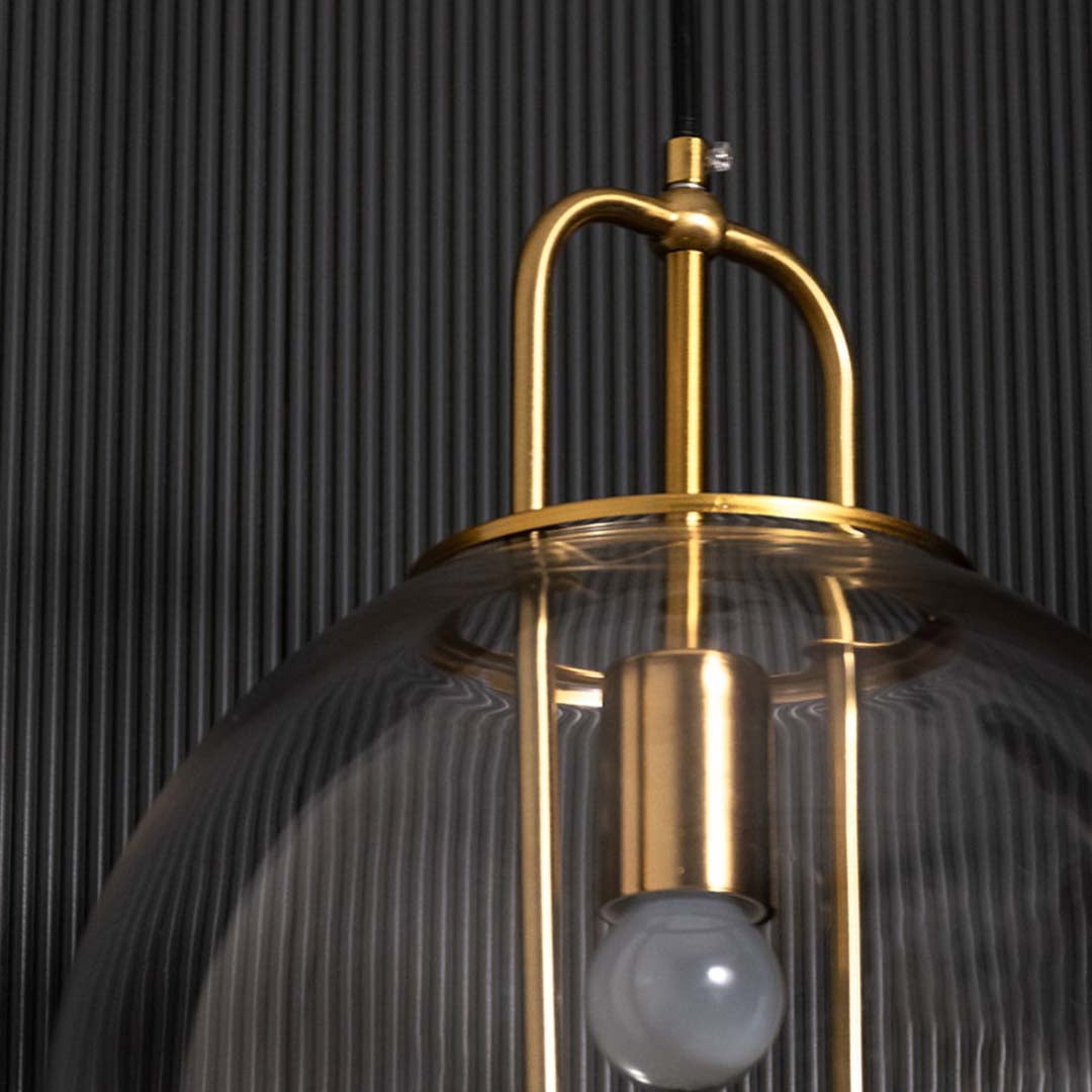 Closeup view of the pendant light showing the clear spherical glass shade gold metal rods and inner bulb holder with refined detailing.