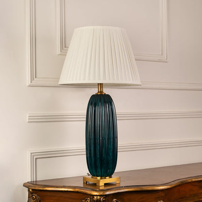 Blue ribbed glass table lamp with white pleated shade and brass accents for elegant bedside and living room decor.