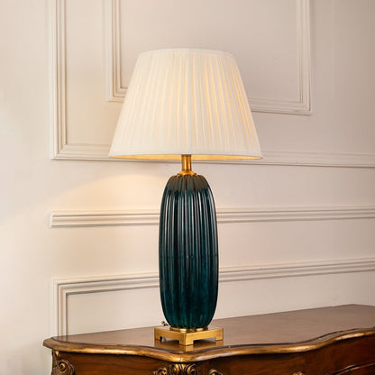 Blue ribbed glass table lamp with pleated shade casting warm ambient light for stylish interior decor settings.