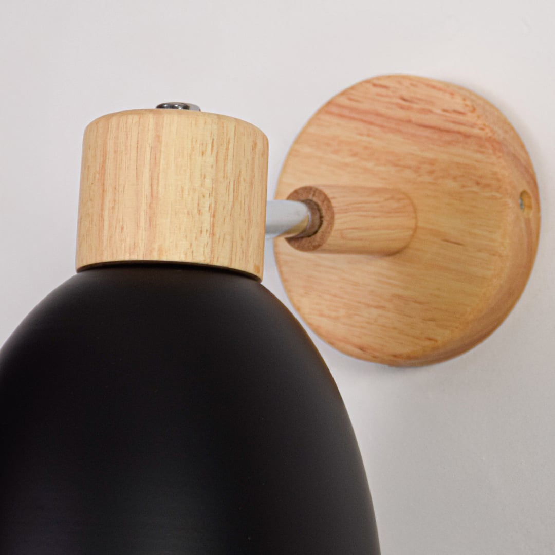 Black metal wall light closeup showing natural wood mount and smooth matte shade finish for modern interior decor.