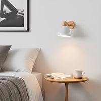 Modern wall light with white metal shade and wooden base mounted beside bed creating warm ambient lighting for calm bedroom reading space.