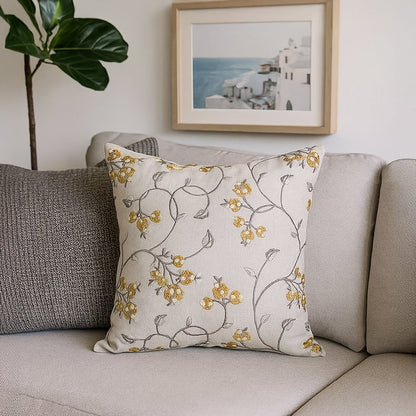 Beige cotton cushion cover with yellow floral embroidery styled on a couch creating a cozy nature inspired décor setting with a soft durable and skin friendly material.