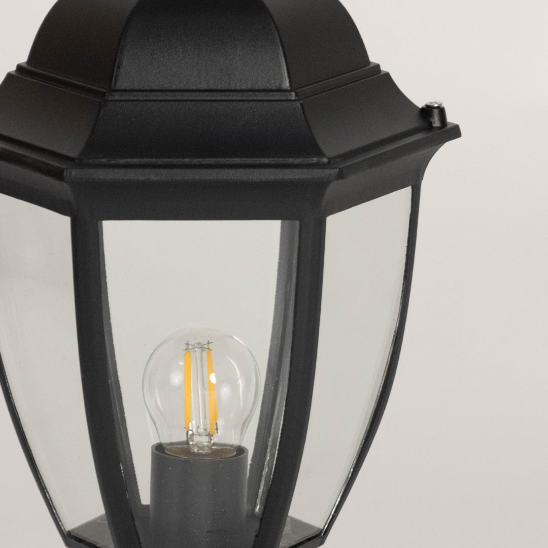 Closeup of outdoor black pillar lamp featuring transparent glass panels and LED bulb design with sleek modern finish.