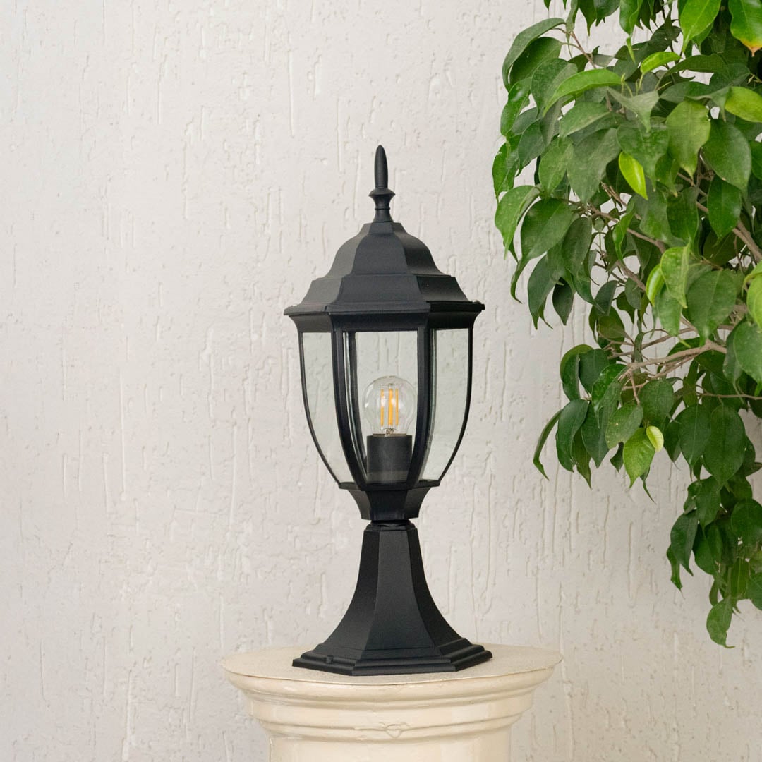 Classic outdoor black pillar lamp with transparent glass shade placed on stone pillar perfect for villa entrance decor.