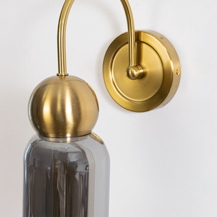 Closeup of gold metal wall light with smoked grey glass shade highlighting smooth curved design and elegant finish.