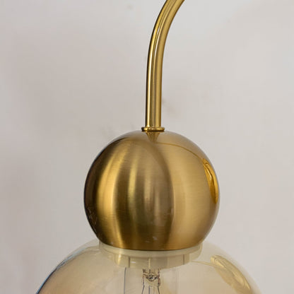 Closeup of gold metal wall light with amber glass globe shade highlighting smooth curved shape and elegant finish.