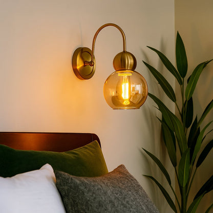 Gold metal wall light with amber glass globe shade adding warm ambient lighting to a modern home interior.