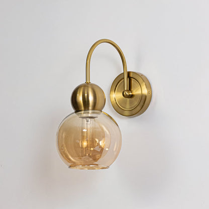Gold metal wall light with amber glass globe shade shown on a white background for clear product detailing.