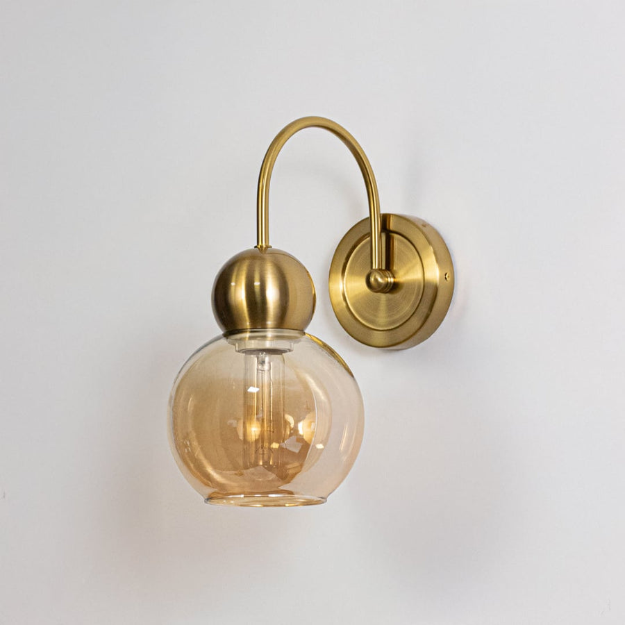 Gold metal wall light with amber glass globe shade shown on a white background for clear product detailing.