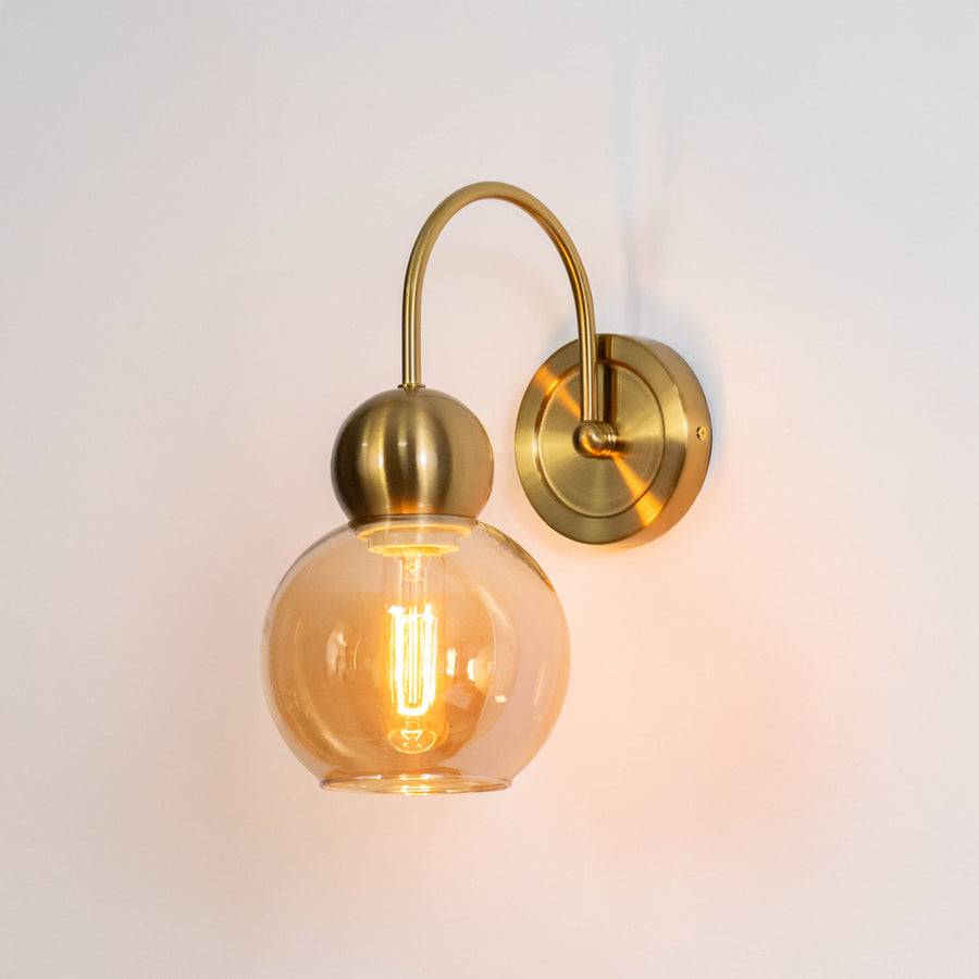 Modern wall light in gold metal finish with glass globe shade for bedroom or living room decor lighting white background.