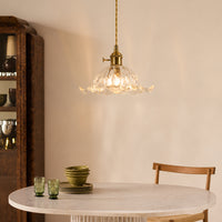 Brass metal and clear glass pendant light adding warm elegance above the dining table in interiors.