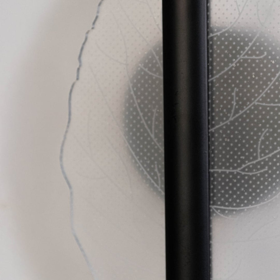 Closeup of black wall light with leaf shaped acrylic acrylic shade highlighting textured leaf pattern and sleek finish.