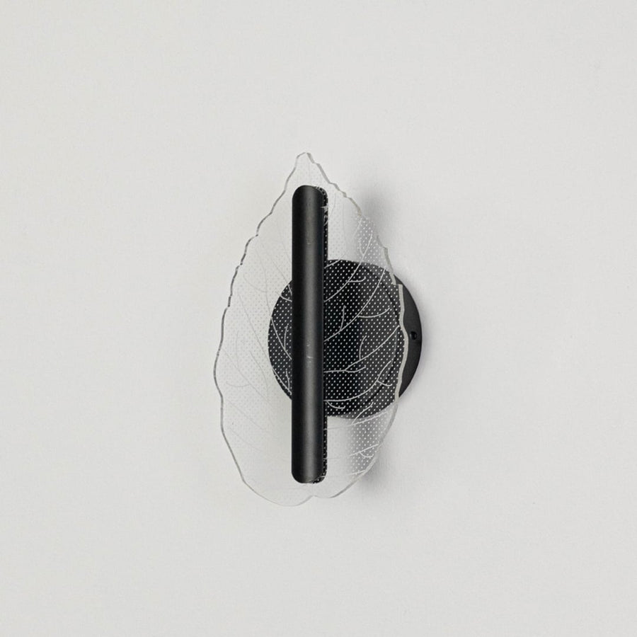 Black wall light with leaf shaped acrylic shade shown on a bright white background with lights off for product clarity.